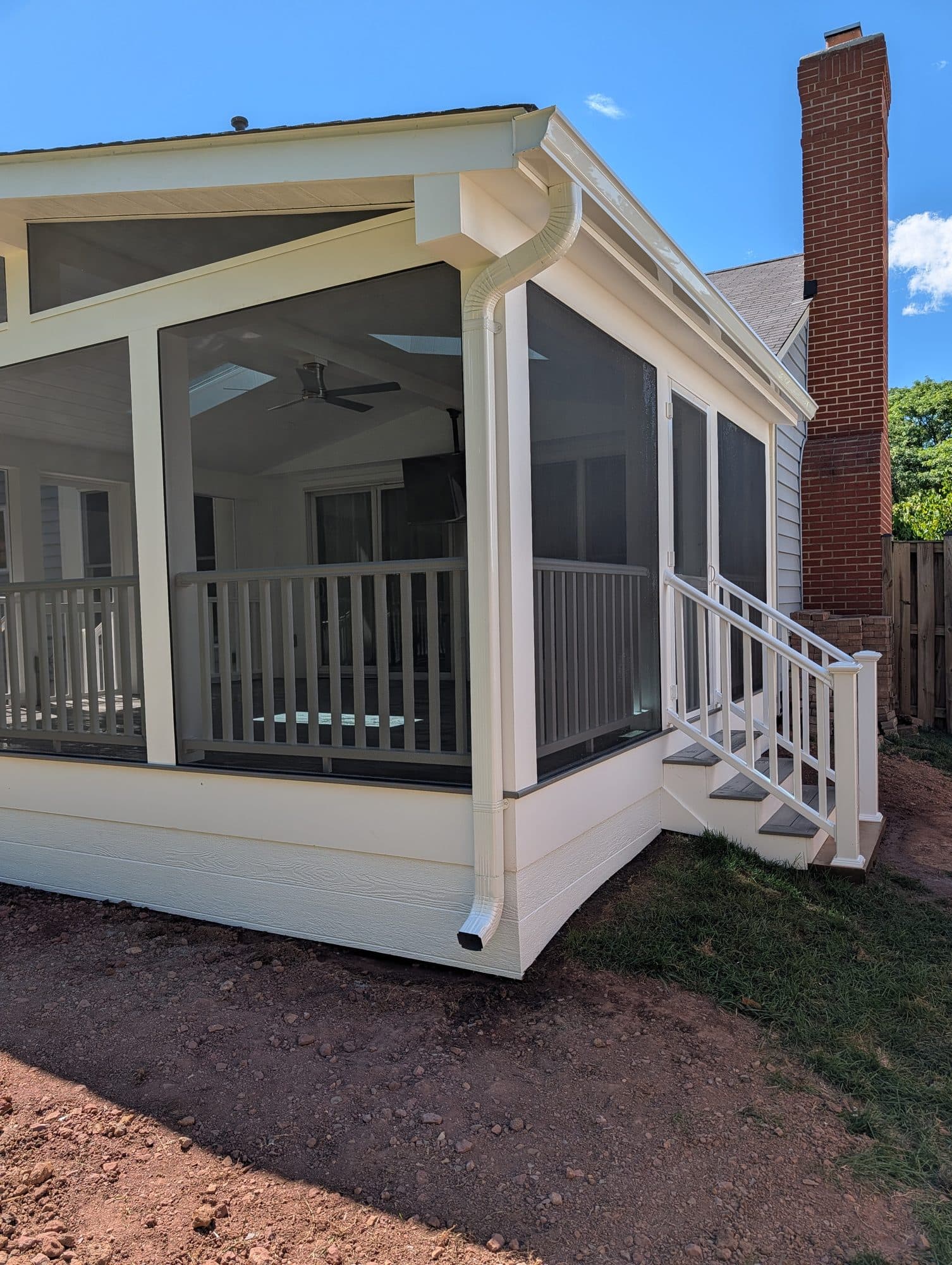 Screened-in porch exterior corner with stairs and railing, brick chimney in background