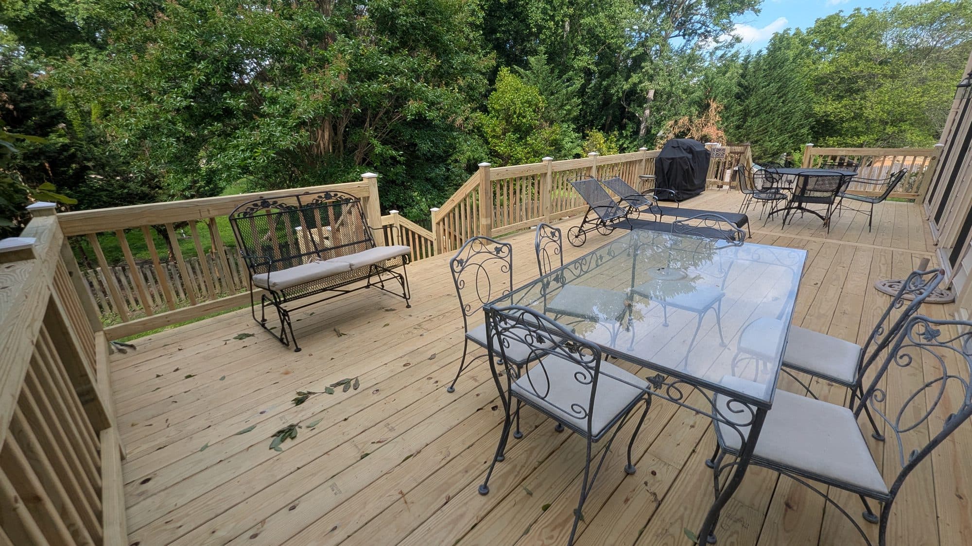 Wood deck with wrought-iron patio furniture overlooking a wooded backyard